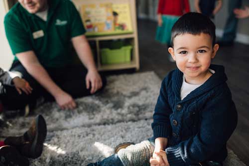 A child on a carpet in a nursery, smiling at the camera