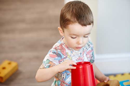 A preschool child looks over his tower made of plastic cups