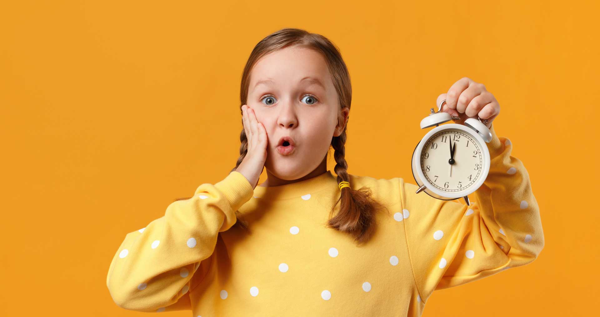A girl holding an analogue alarm clock looking fake-shocked