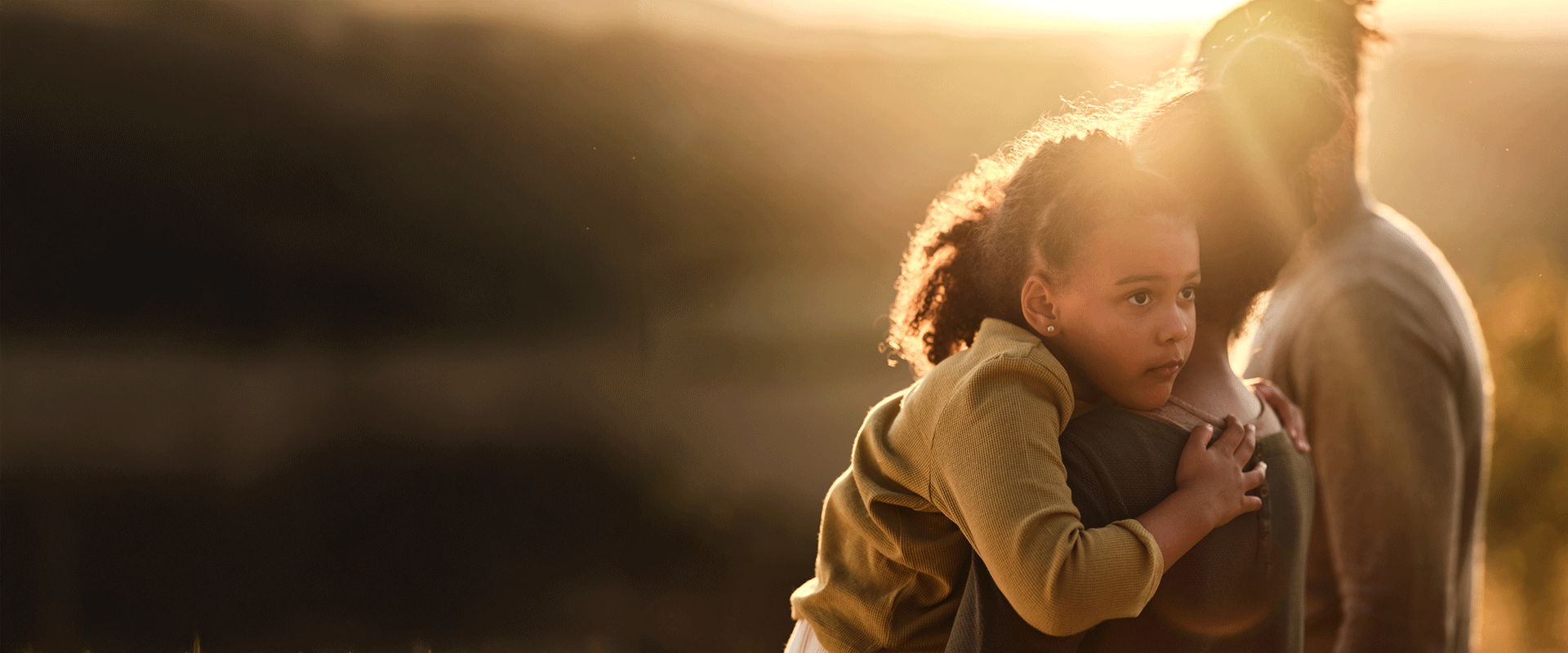 A mother and young daughter sit at the top of their garden steps, facing away from camera. The mother appears to be comforting the daughter.