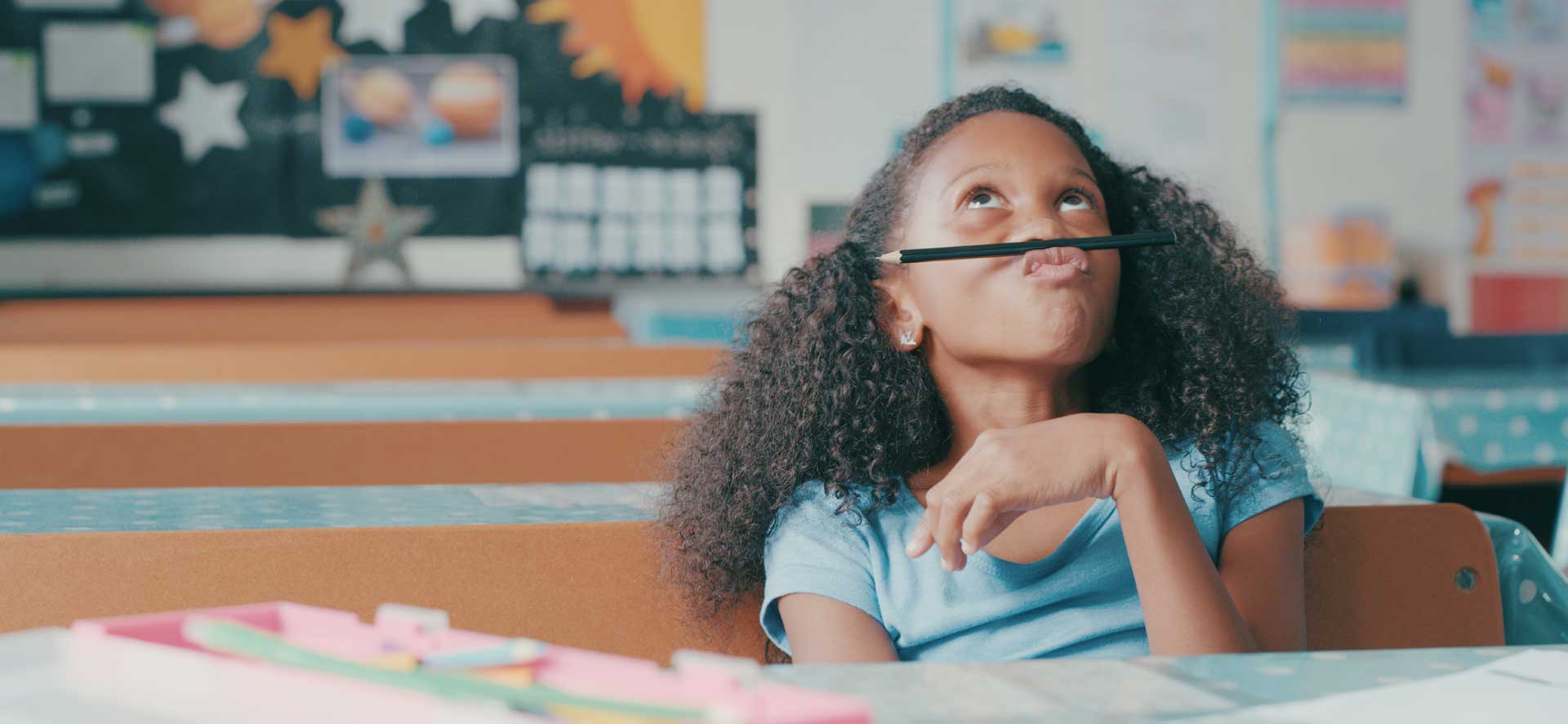 A child is distracted in class, and has resorted to attempting to balance her pencil under her nose.