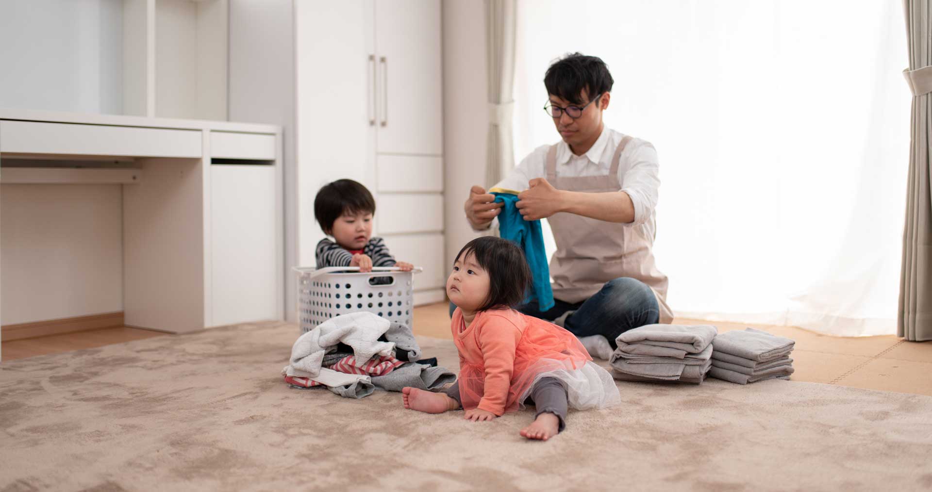 A father folds laundry as his two young children play and watch