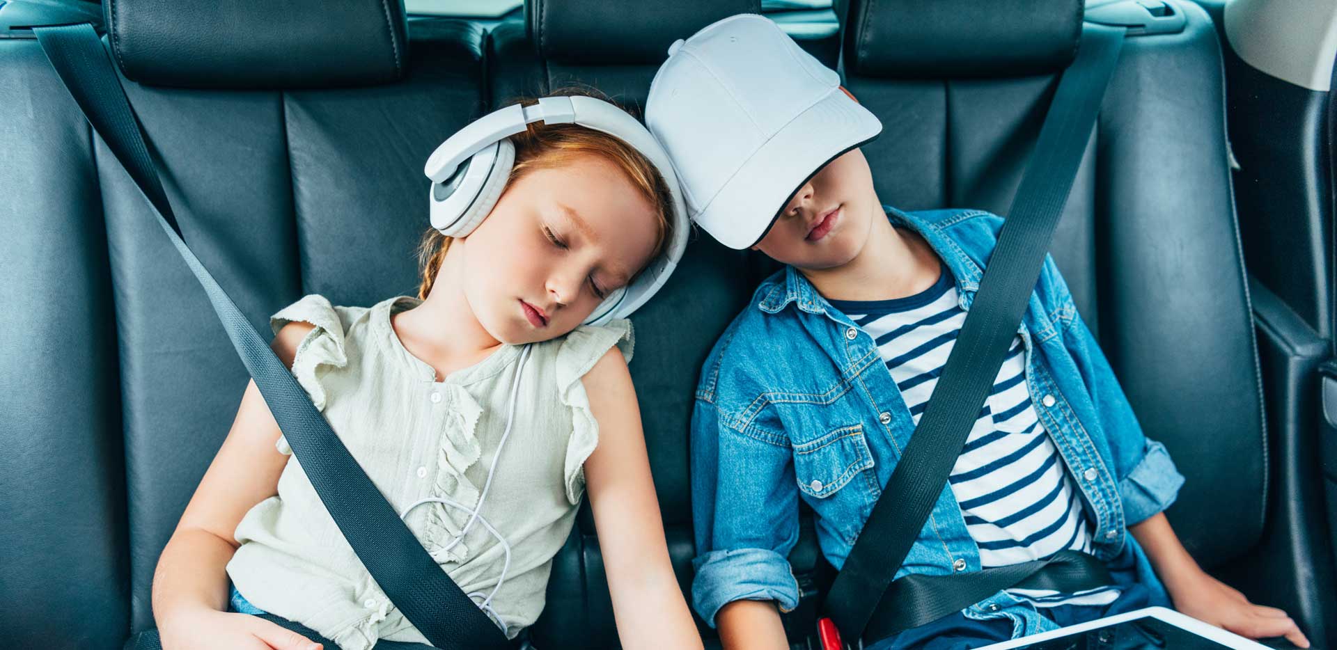 A young brother and sister asleep in the back of a car