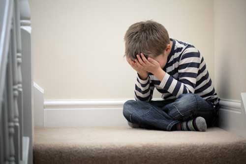 A child with his head in his hands as he sits on the floor
