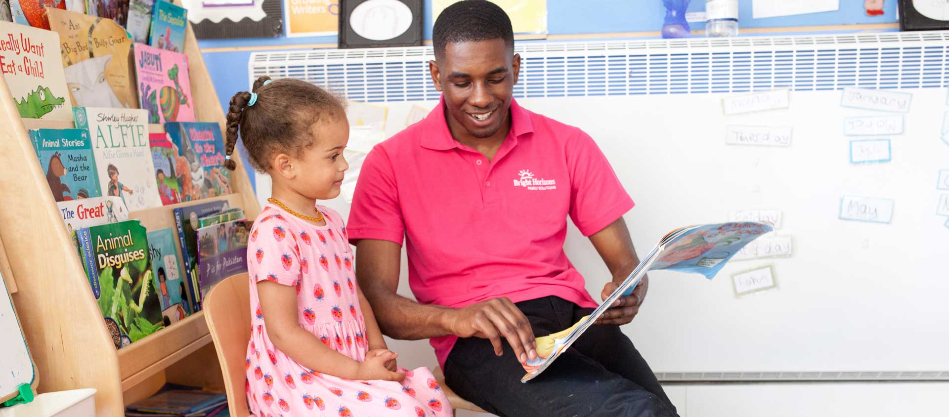 A male nursery worker reads a picture book with a preschool-aged child