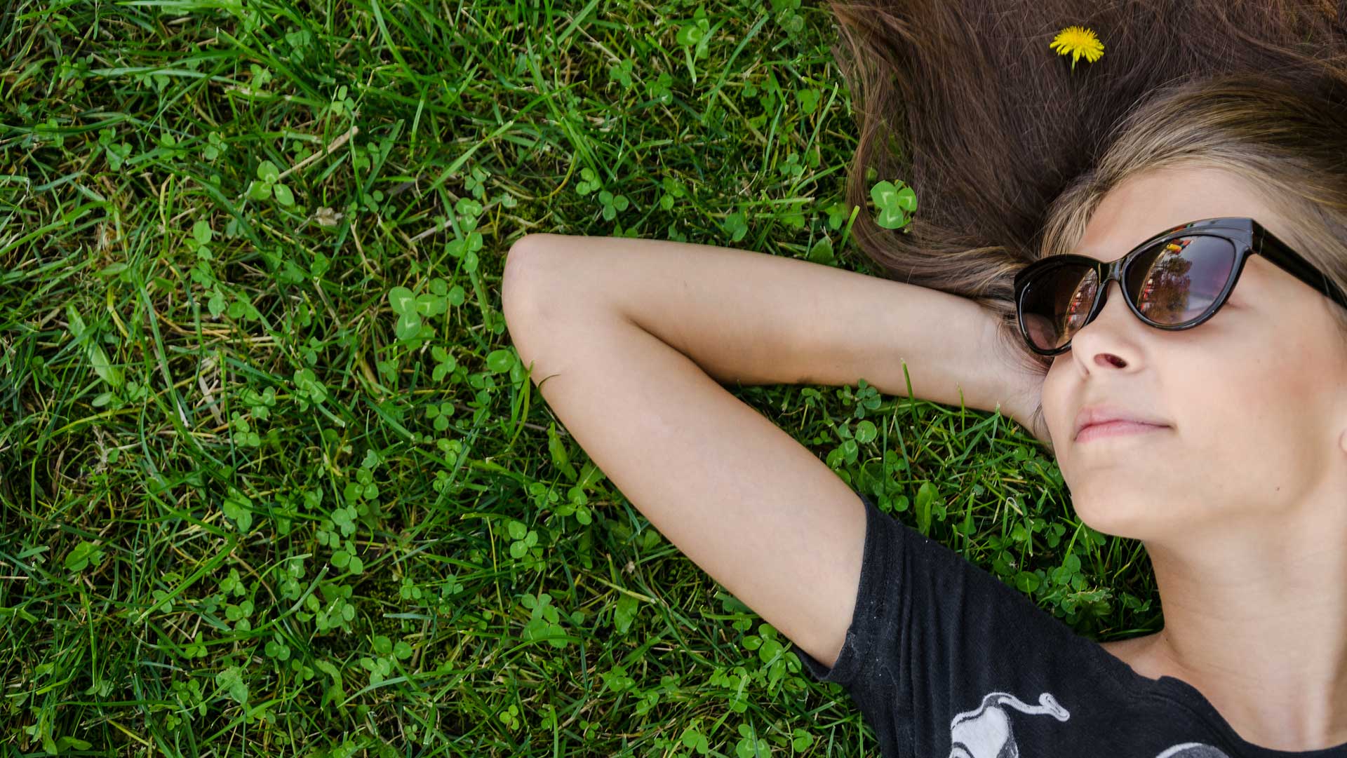 Teenage girl laying in the grass wearing sunglasses and smiling