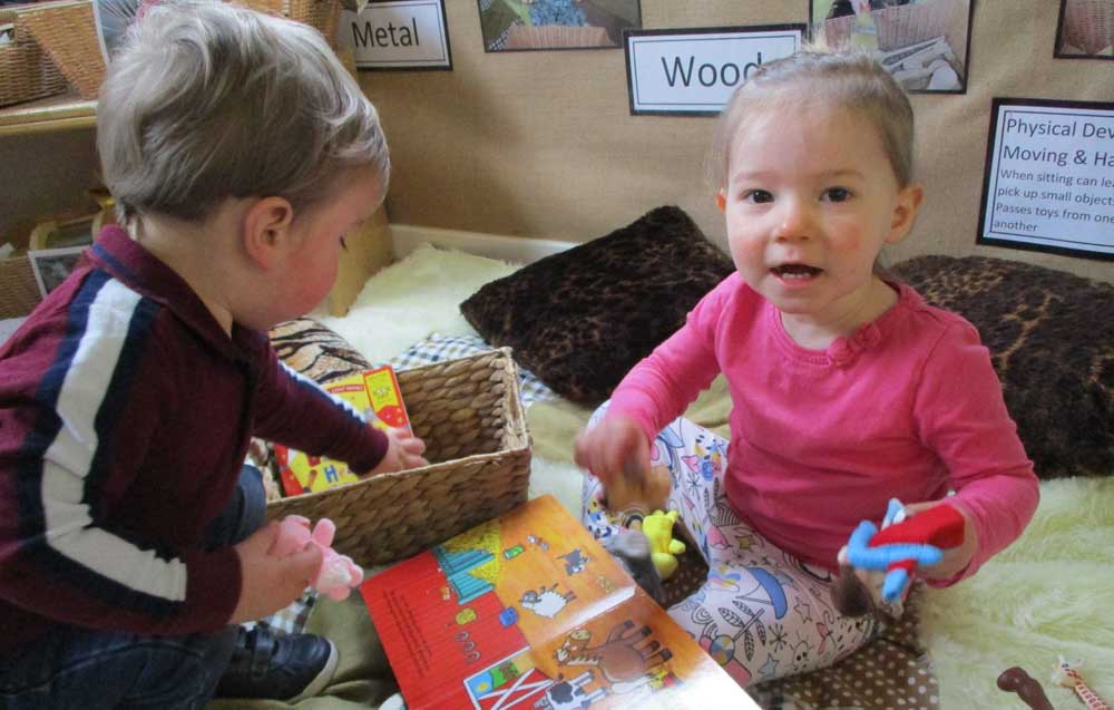 Two toddlers looking at a picture book and playing with farm animal toys