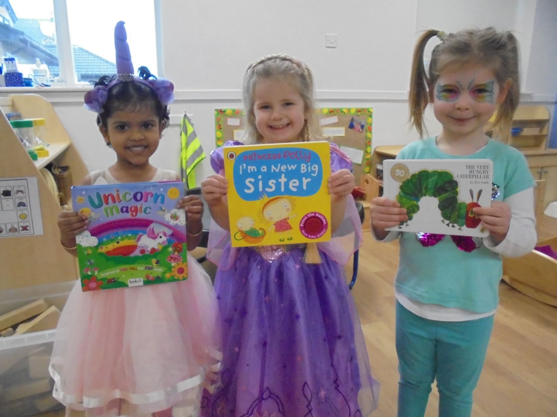 Three young children dressed up as princesses holding up their favourite books for World Book Day