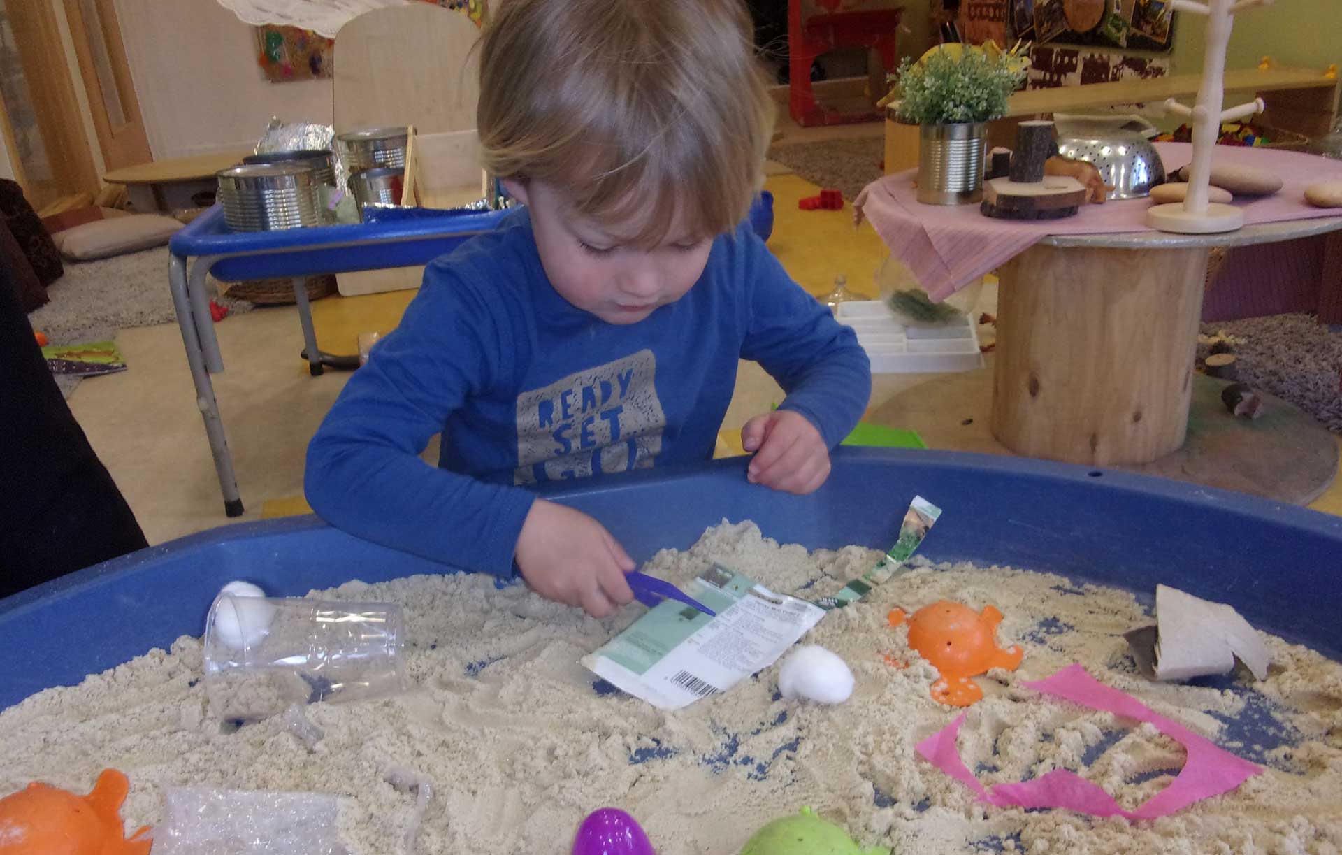 A young child plays in a sand box that replicates sea-life (including the current environmental pollution of plastic)