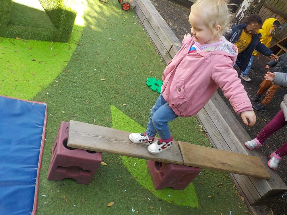 A young child "walks the plank" across a balance beam