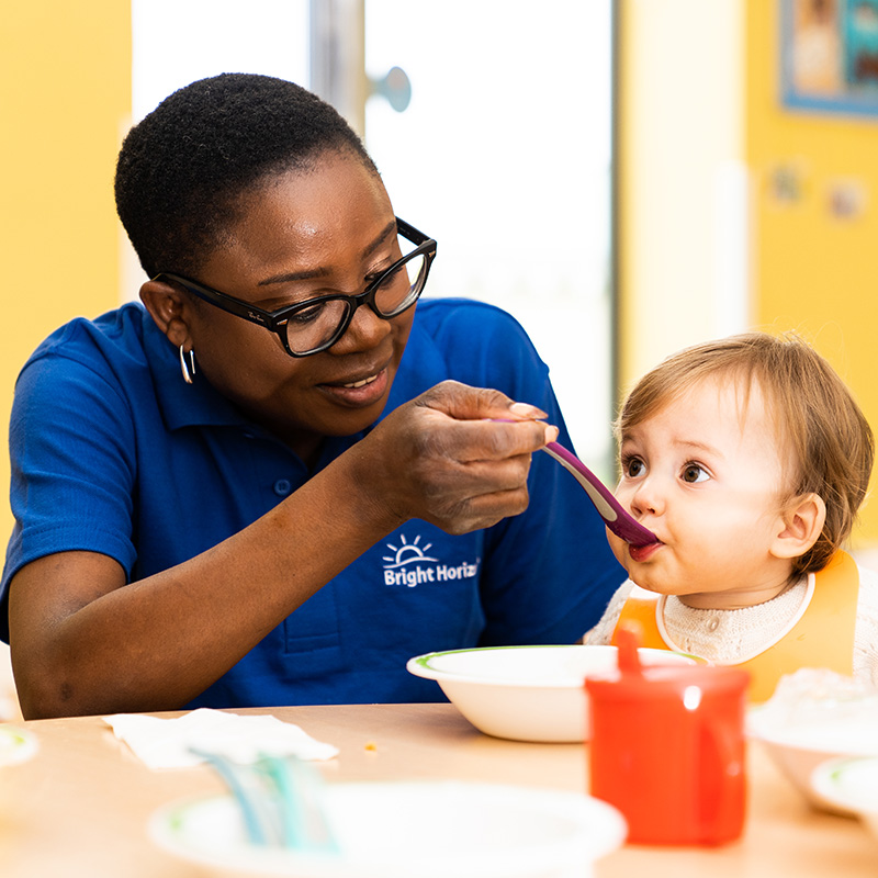 Member of staff spoon feeding baby