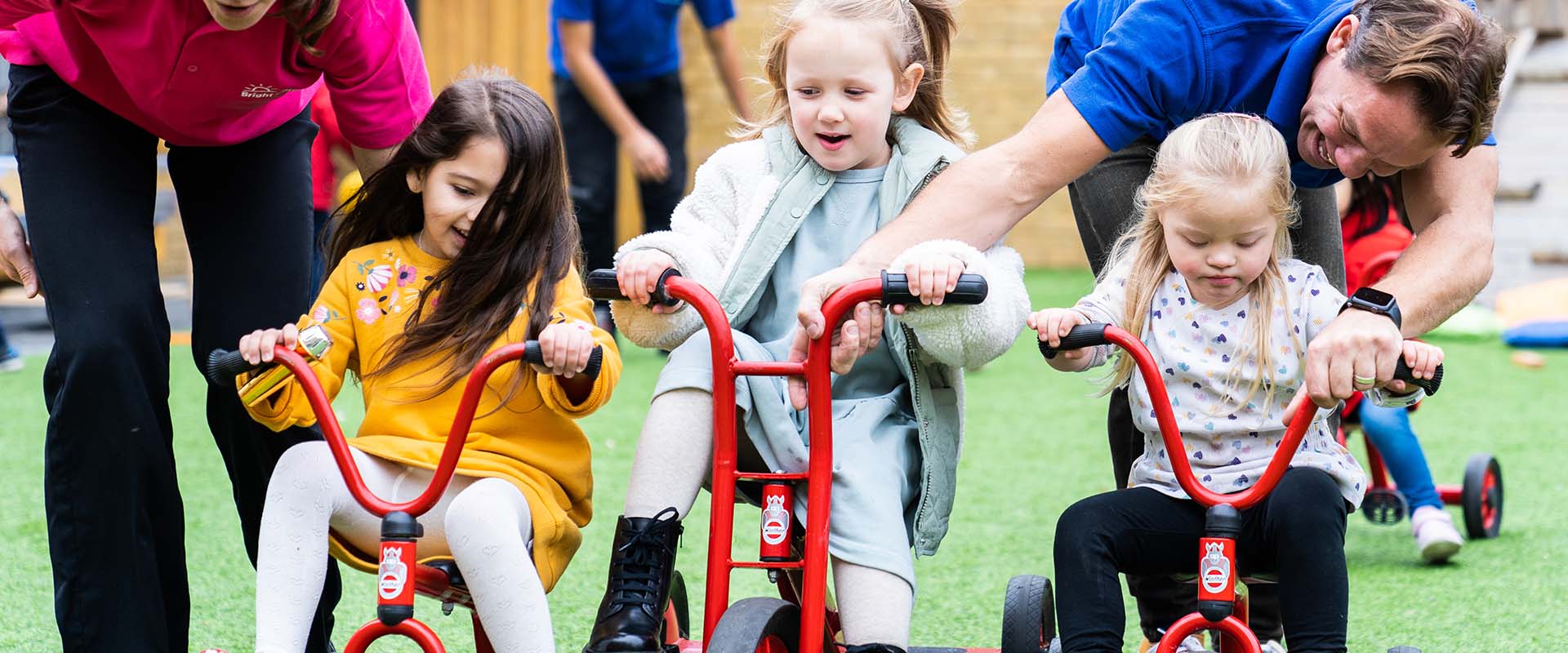 Pre-school children riding tricycles outside in nursery garden