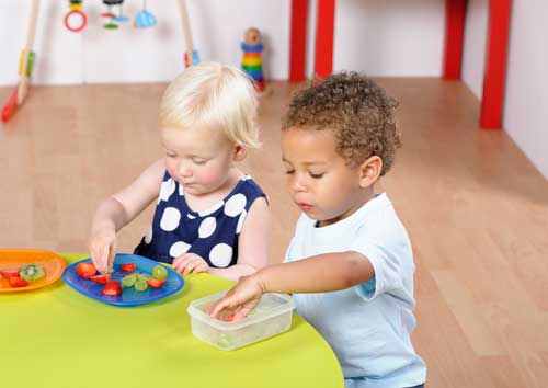 Two toddlers in nursery eating fruit