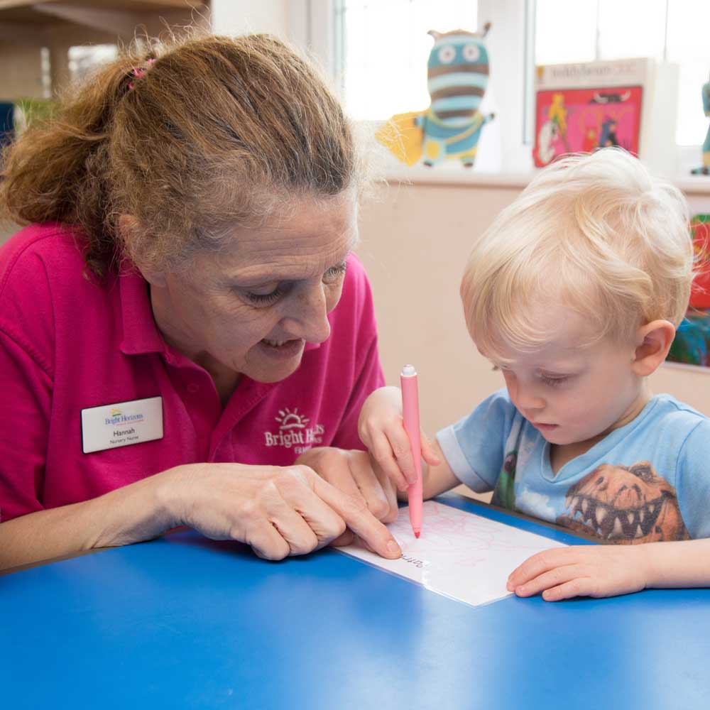 A member of nursery staff helps a young child practice his writing skills.