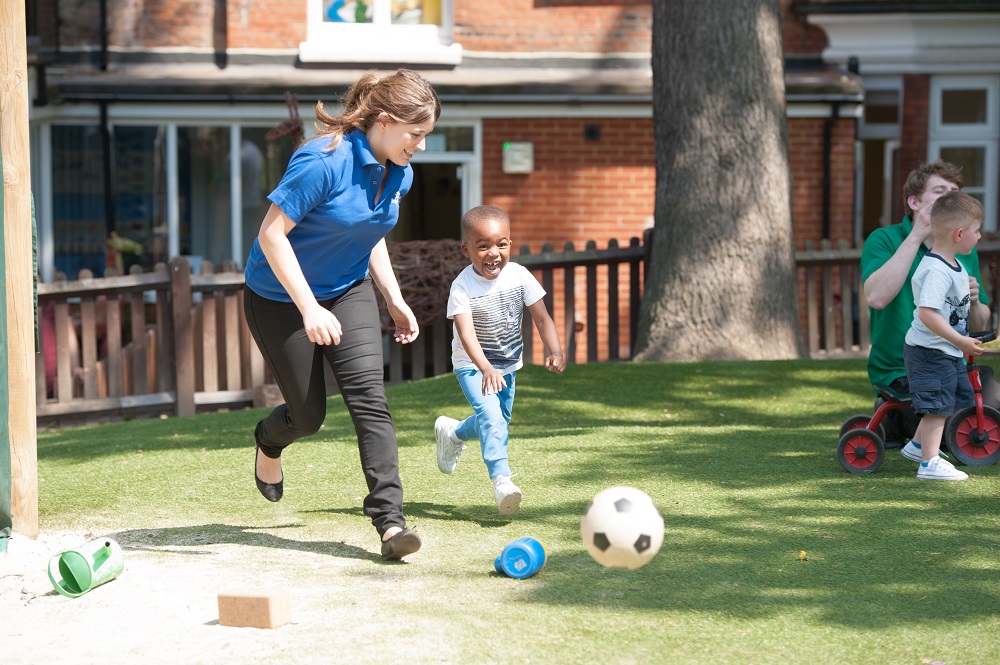 A Bright Horizons staff member plays football with a child