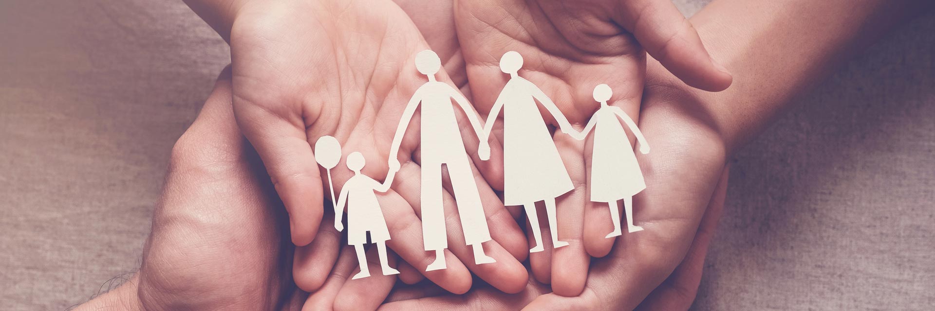 Adult hands holding a child's hands holding a paper cutout of a family