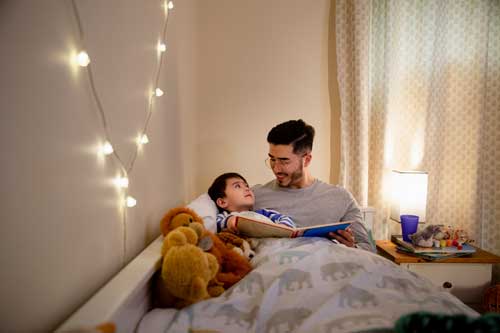 A small child and his father in the child's bed reading a book together