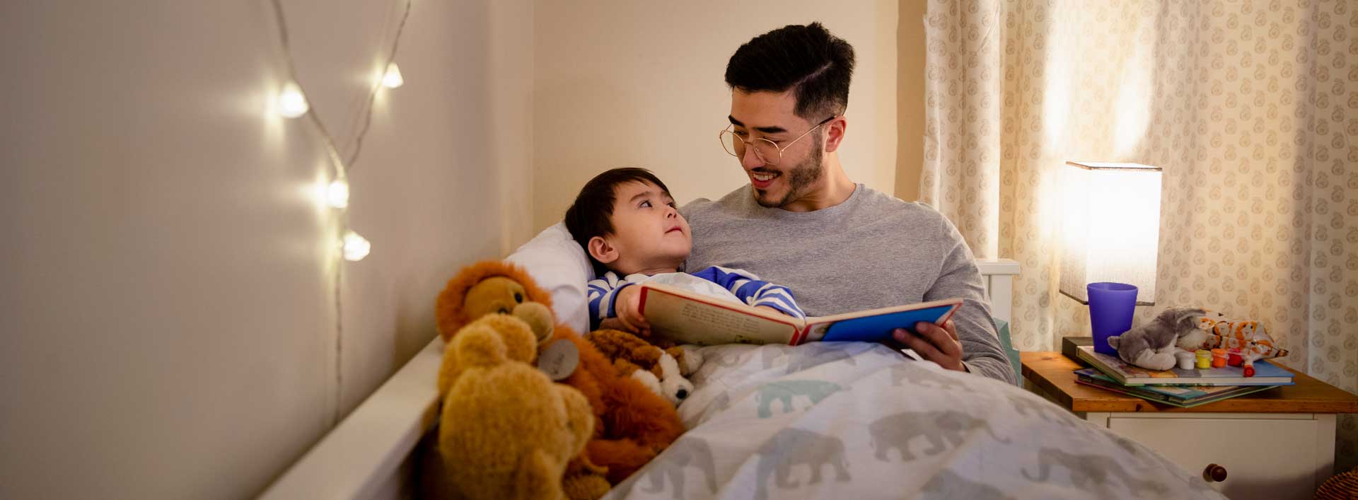 A small child and his father in the child's bed reading a book together