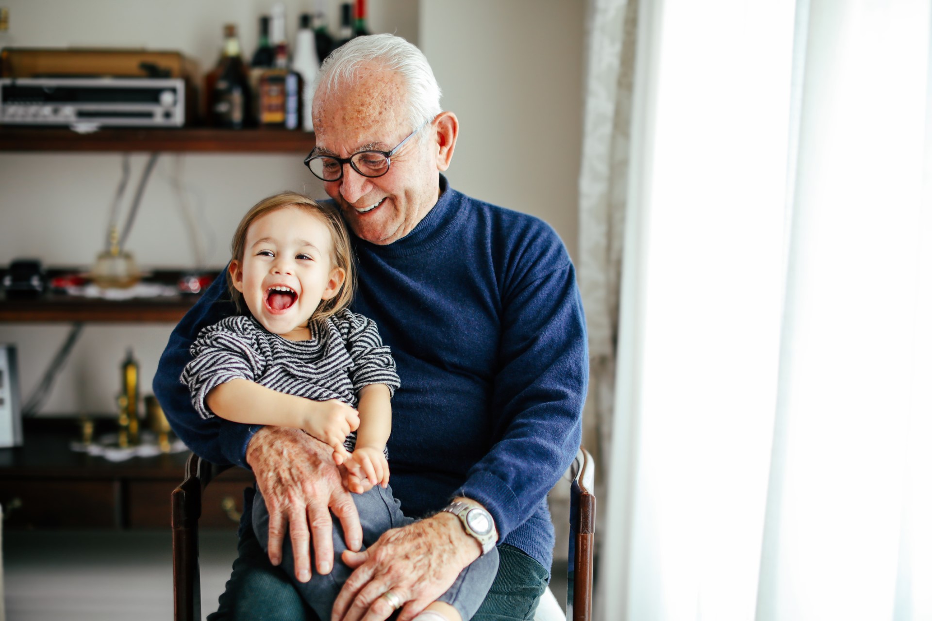 Grandfather smiling holding young grandchild who is laughing