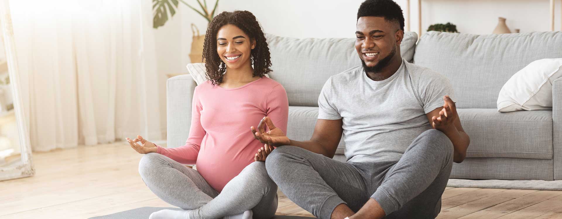 A man and his pregnant partner doing yoga in their living room together