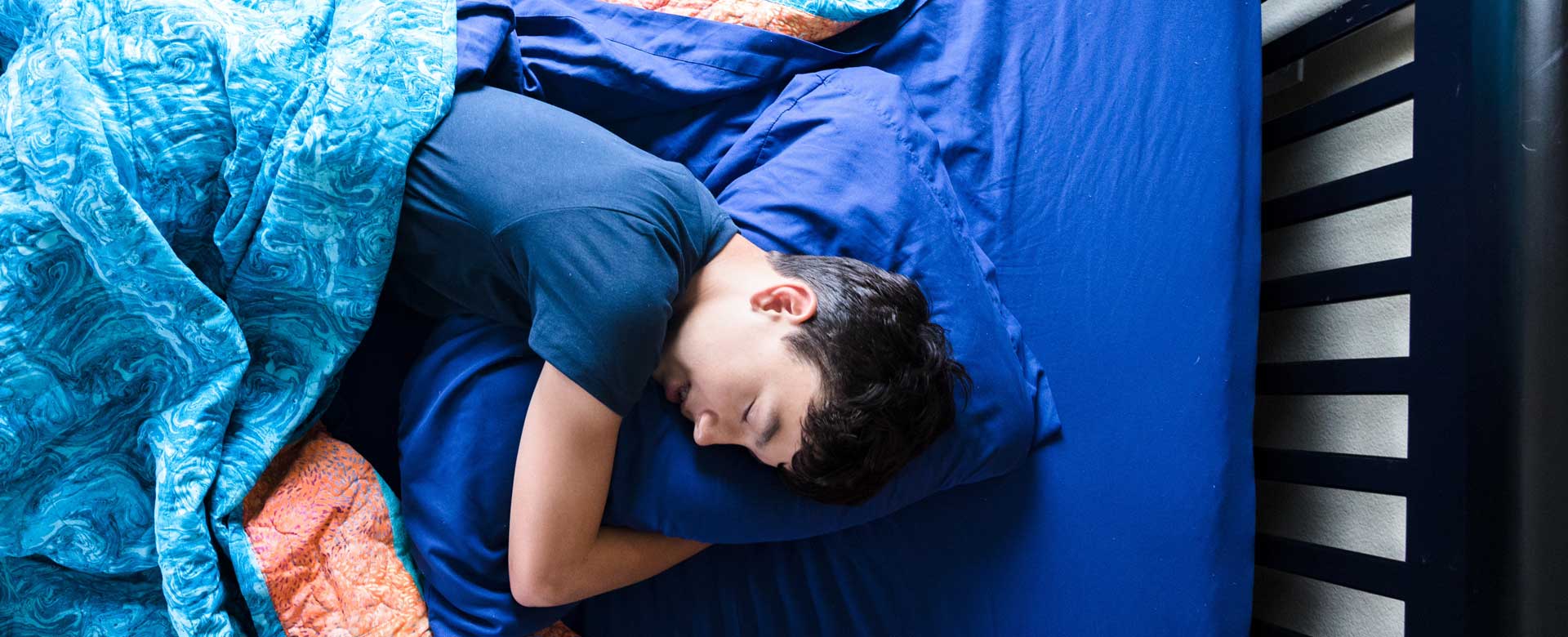A teenager hugs his pillow as he sleeps in his bed