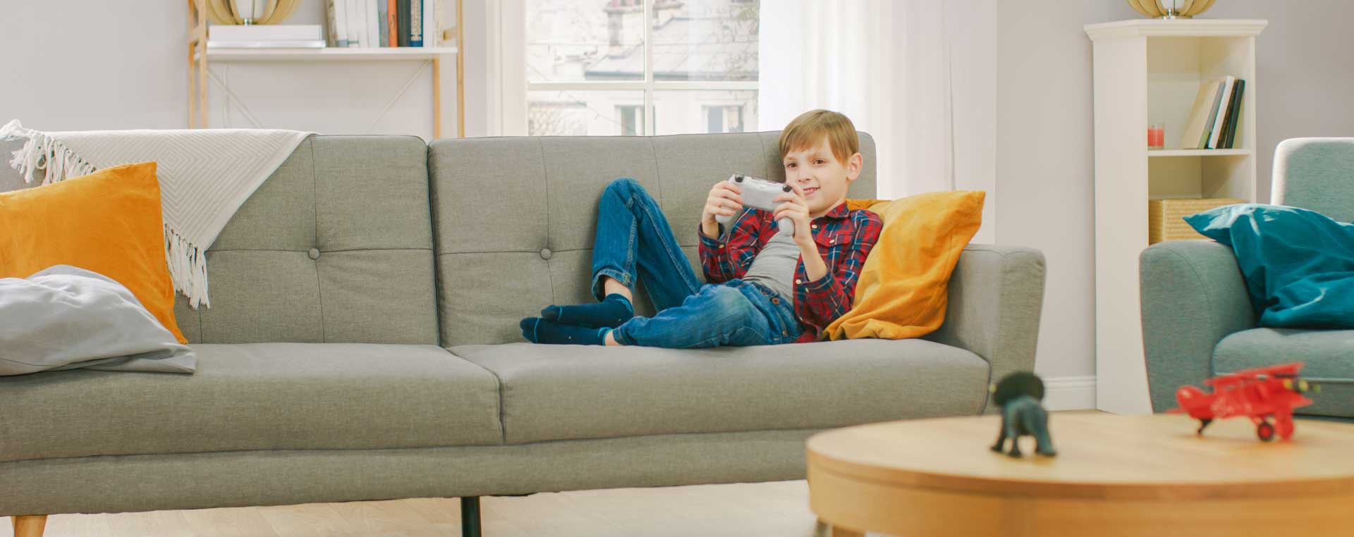 A boy sits on a sofa with his feet up, playing Playstation