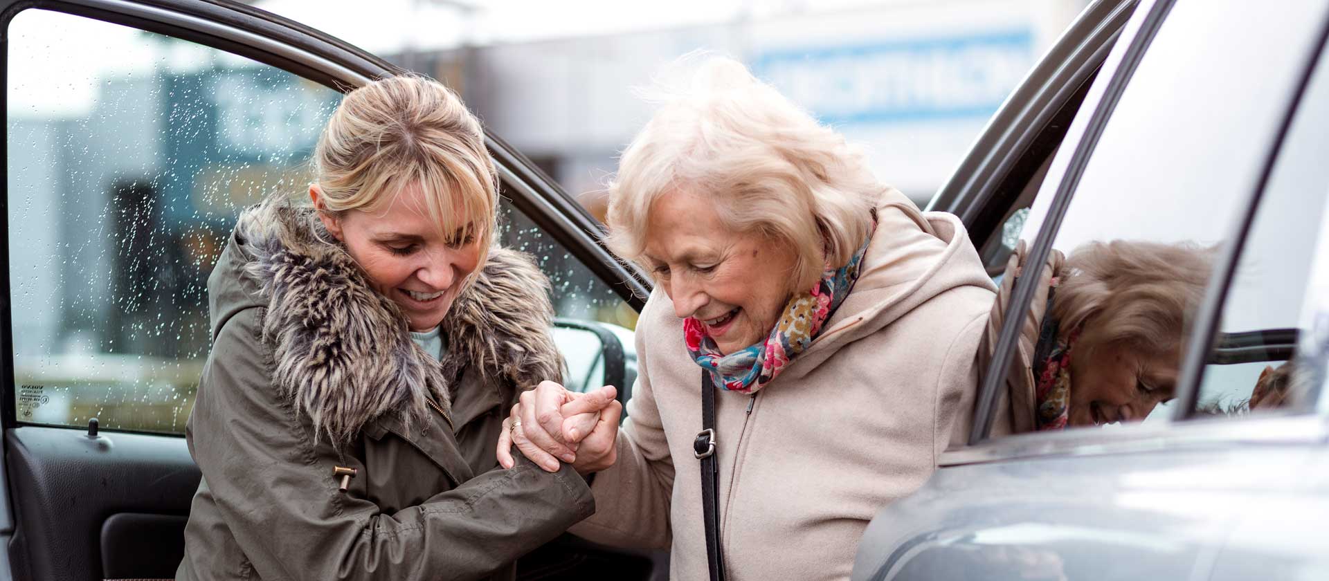 A lady helps her elderly mother out of a car