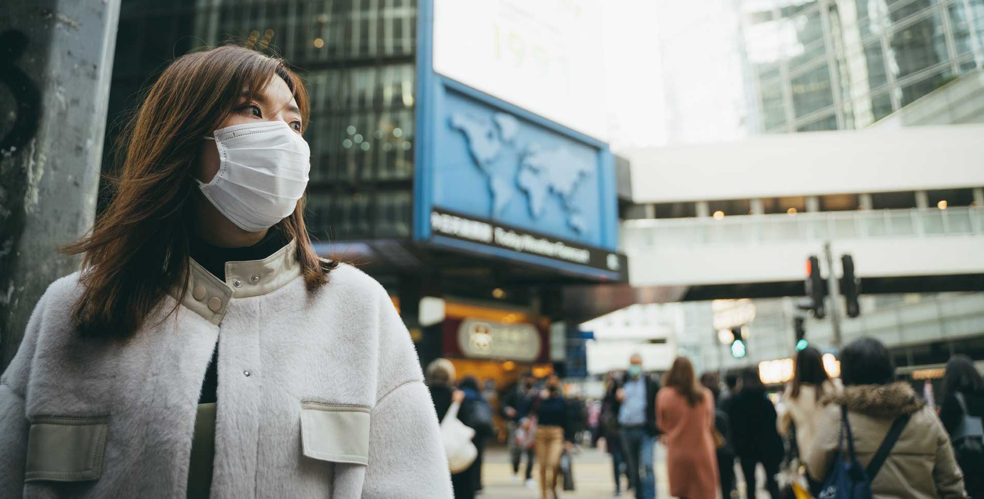 An Asian lady in a facemask in a crowded city